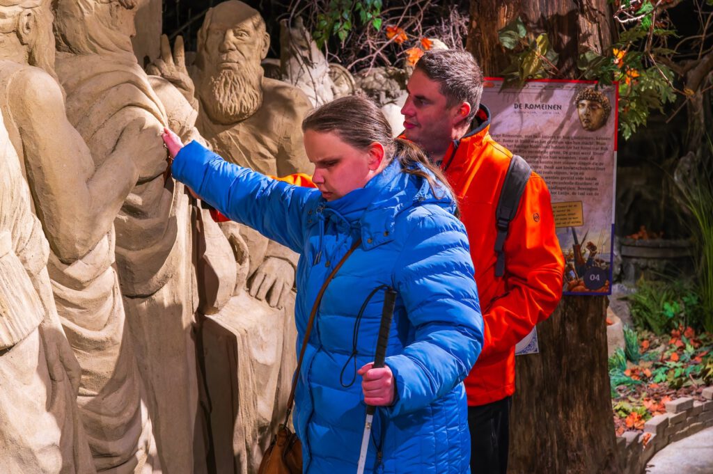 Een blinde dame verkent me haar handen een zandsculptuur 